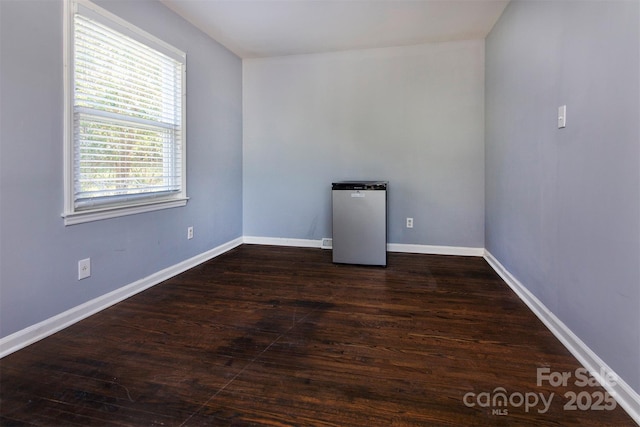 spare room with baseboards and dark wood-style floors