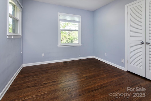 unfurnished bedroom with a closet, dark wood-type flooring, visible vents, and baseboards