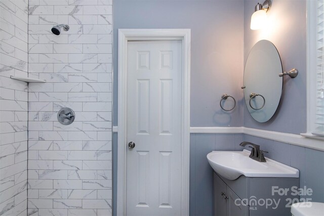 full bath featuring tiled shower, vanity, toilet, and wainscoting