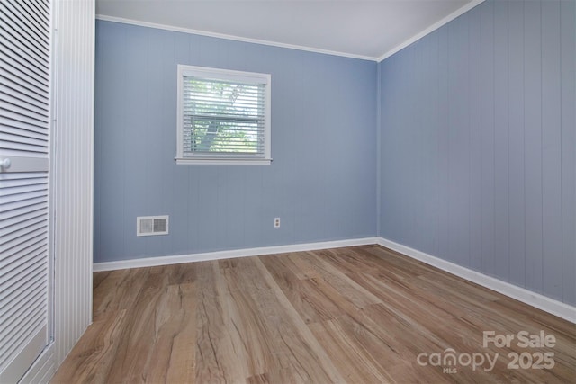 unfurnished room with crown molding, wood finished floors, baseboards, and visible vents