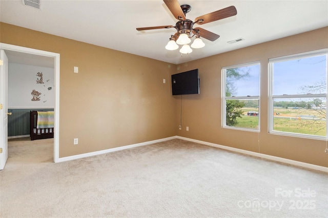 empty room featuring light colored carpet, a ceiling fan, visible vents, and baseboards