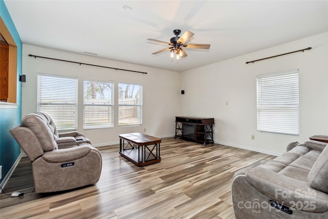 living room featuring baseboards, a ceiling fan, and light wood-style flooring