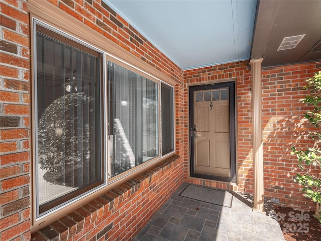 doorway to property with brick siding and visible vents