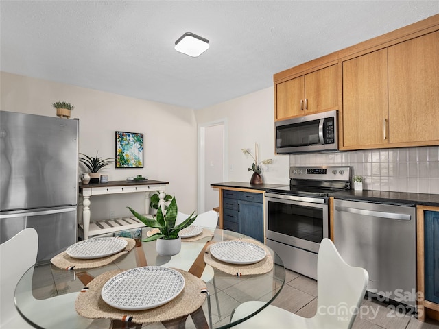 kitchen with light tile patterned floors, stainless steel appliances, backsplash, and dark countertops