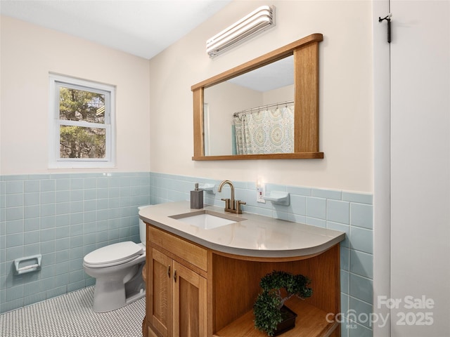full bath with tile patterned floors, toilet, vanity, wainscoting, and tile walls