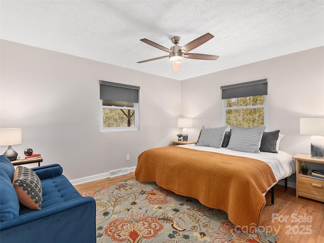bedroom with baseboards, visible vents, wood finished floors, and a textured ceiling
