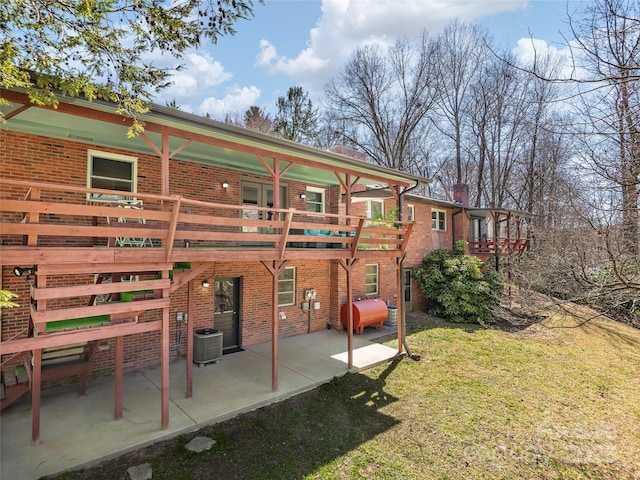 back of property with cooling unit, a lawn, heating fuel, and brick siding