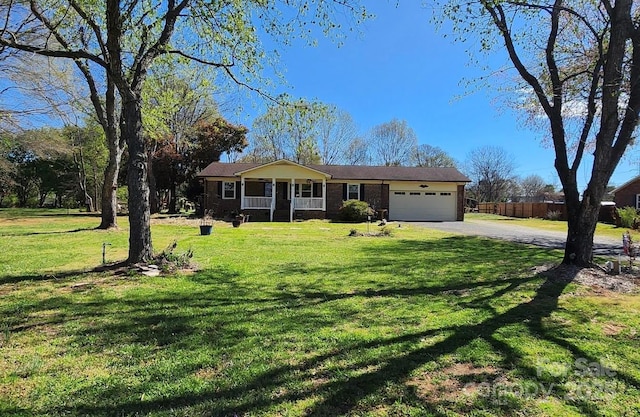 ranch-style house featuring driveway, covered porch, an attached garage, fence, and a front yard