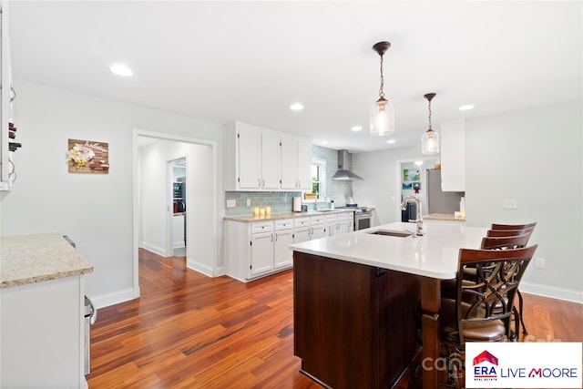 kitchen featuring white cabinets, dark wood finished floors, light countertops, a sink, and wall chimney exhaust hood