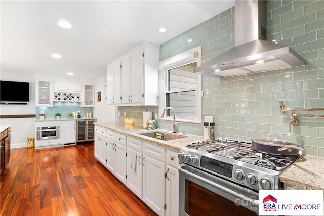 kitchen with wall chimney exhaust hood, stainless steel appliances, white cabinets, a sink, and decorative backsplash