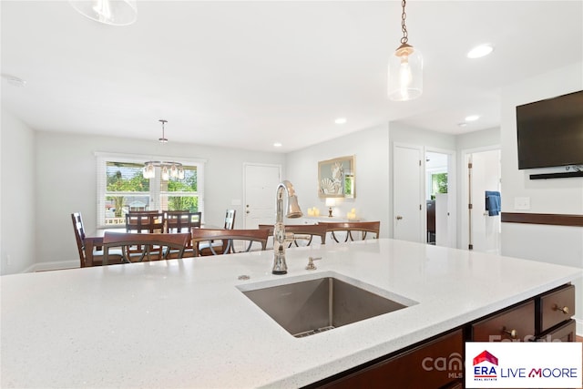 kitchen featuring dark brown cabinets, light stone countertops, decorative light fixtures, and a sink