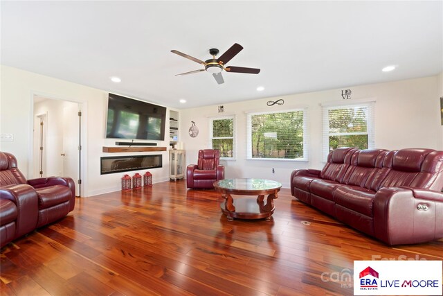 living area featuring a ceiling fan, a glass covered fireplace, wood finished floors, and recessed lighting