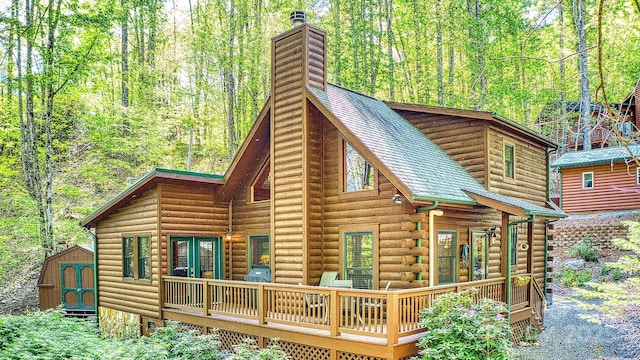 rear view of house with a wooden deck, a chimney, roof with shingles, and a wooded view