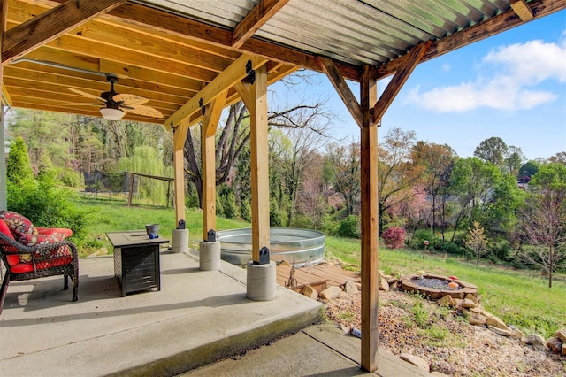 view of patio with fence, a ceiling fan, a fire pit, and an outdoor hot tub