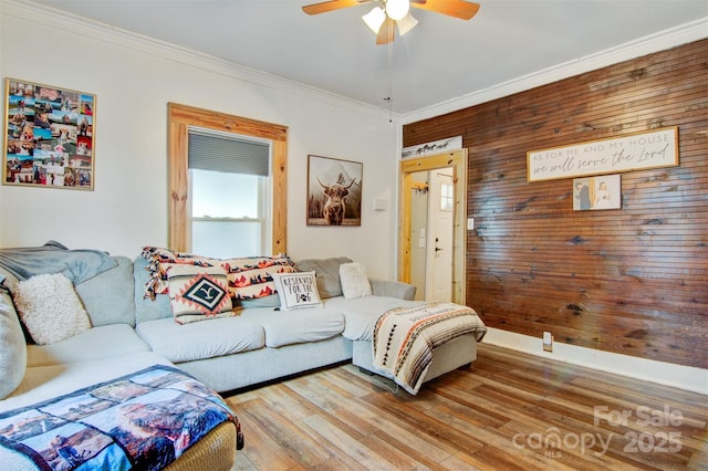 living area with ornamental molding, ceiling fan, light wood-style floors, and wood walls