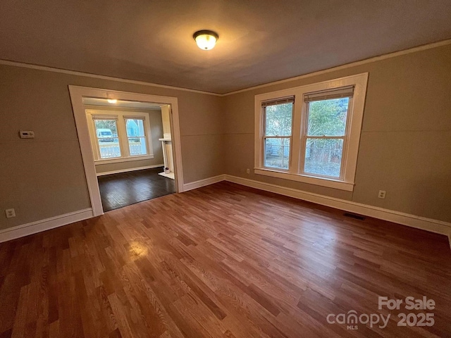 empty room featuring dark wood-style flooring, plenty of natural light, baseboards, and visible vents