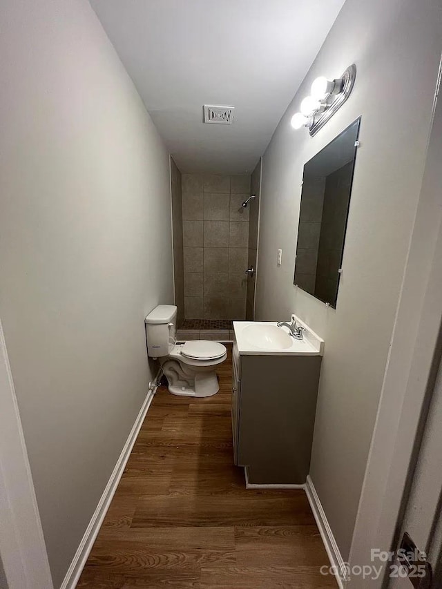 full bath featuring vanity, toilet, visible vents, tiled shower, and wood finished floors