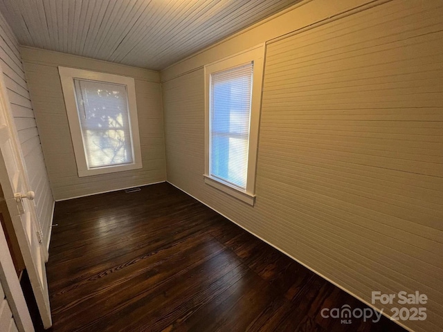 unfurnished room with dark wood-style flooring, visible vents, and a wealth of natural light