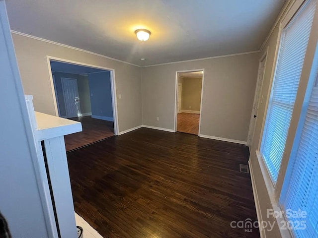 empty room featuring dark wood-type flooring, baseboards, ornamental molding, and visible vents
