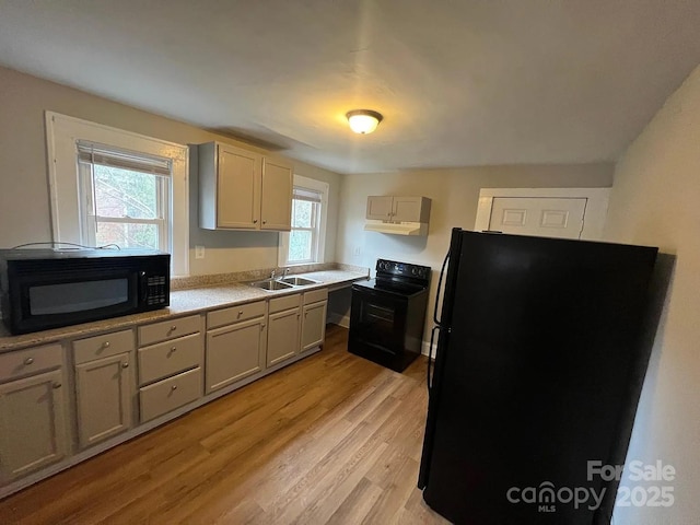 kitchen with light countertops, light wood-style flooring, under cabinet range hood, a sink, and black appliances