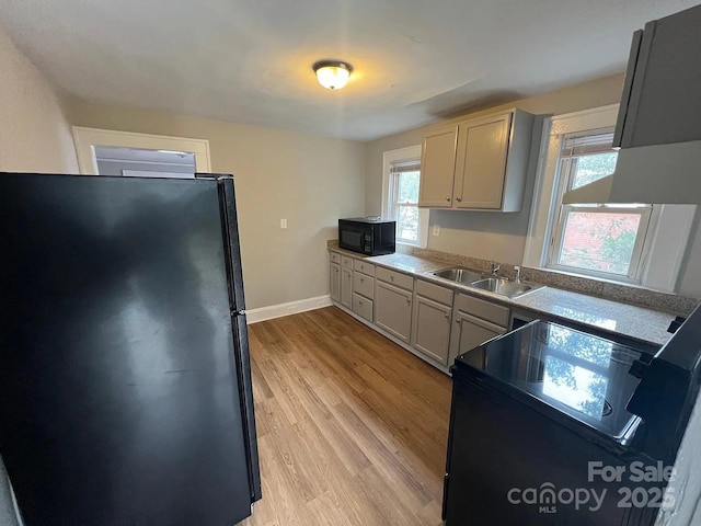 kitchen with baseboards, black appliances, light wood-style floors, and a sink