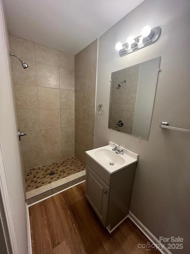 full bathroom featuring a tile shower, wood finished floors, and vanity