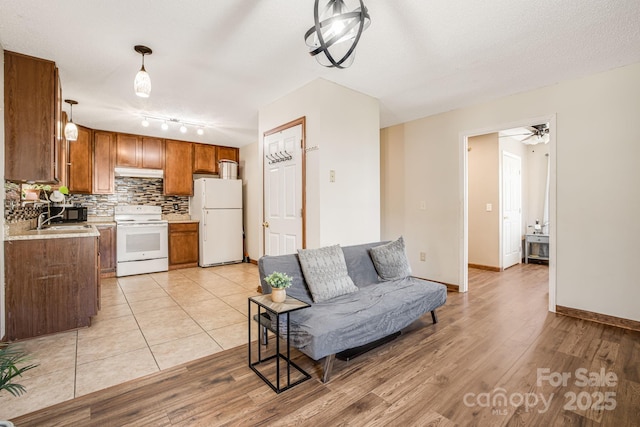 kitchen featuring tasteful backsplash, white appliances, under cabinet range hood, a sink, and brown cabinets