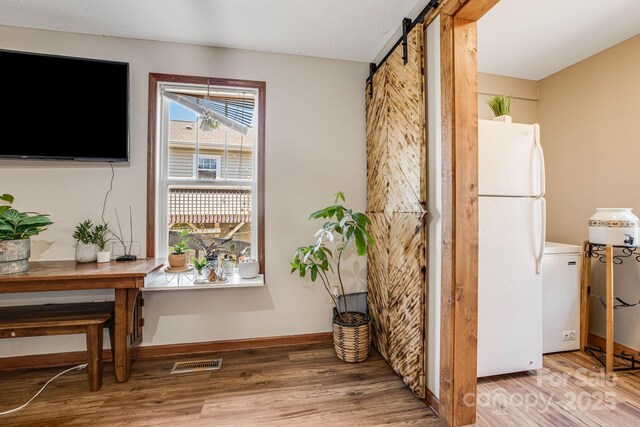 interior space with baseboards, visible vents, a barn door, and wood finished floors