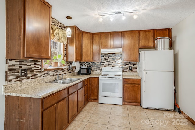 kitchen featuring light tile patterned flooring, a sink, brown cabinetry, under cabinet range hood, and white appliances