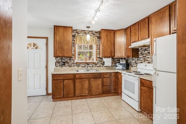 kitchen featuring white appliances, brown cabinetry, under cabinet range hood, and a sink