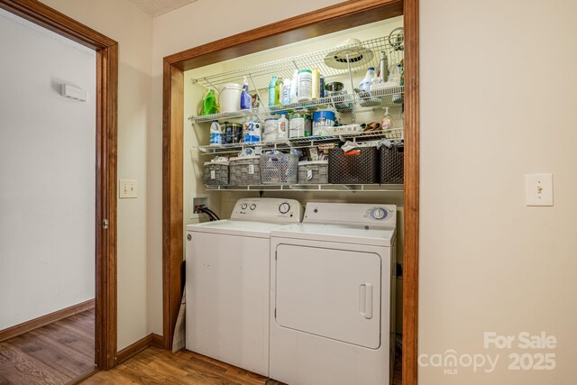 clothes washing area with baseboards, washing machine and dryer, wood finished floors, and laundry area