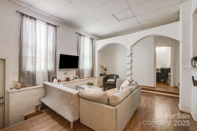 living area featuring a drop ceiling, arched walkways, and wood finished floors