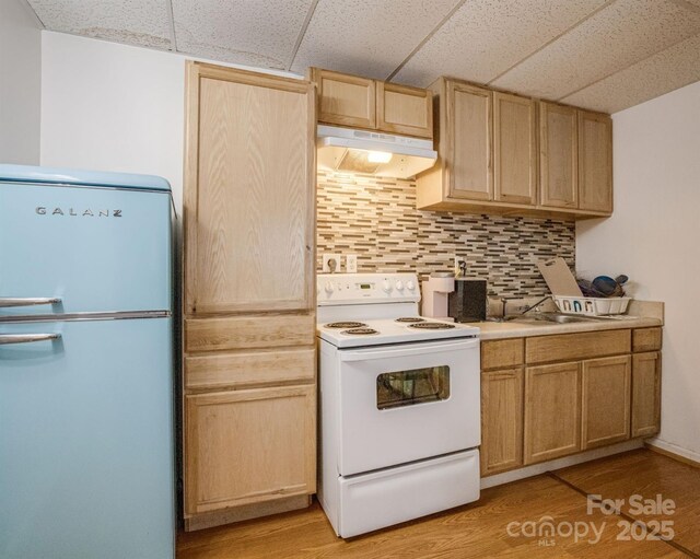 kitchen with tasteful backsplash, white appliances, light brown cabinetry, under cabinet range hood, and light wood finished floors