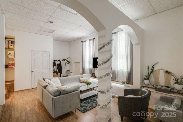 living area with wood finished floors, arched walkways, and a paneled ceiling