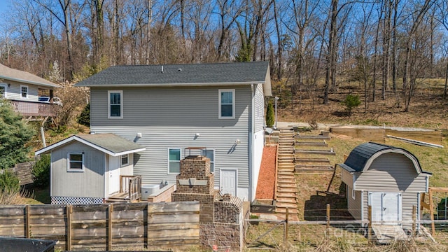 rear view of house featuring a shingled roof, an outdoor structure, and fence private yard