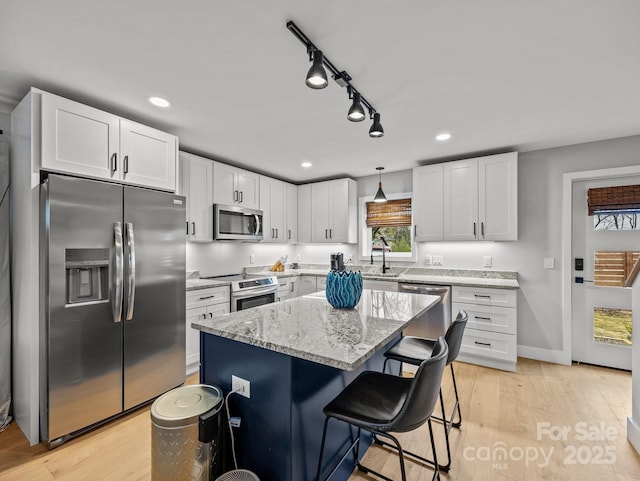kitchen with light stone countertops, a sink, light wood-type flooring, and appliances with stainless steel finishes
