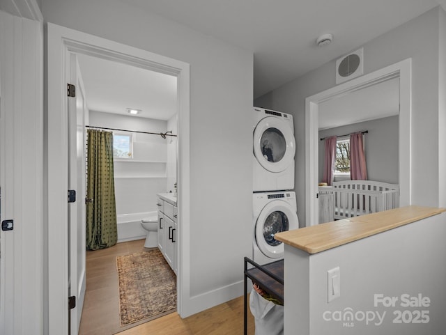 laundry room featuring light wood-type flooring, stacked washer / dryer, laundry area, baseboards, and visible vents