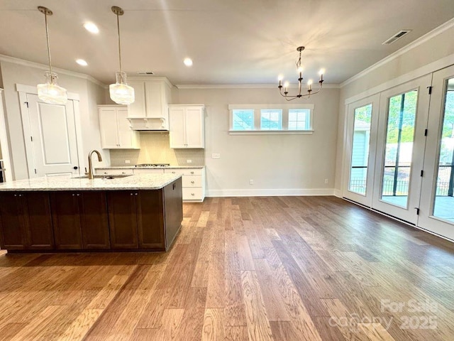 kitchen with stainless steel gas stovetop, wood finished floors, a sink, an inviting chandelier, and white cabinetry