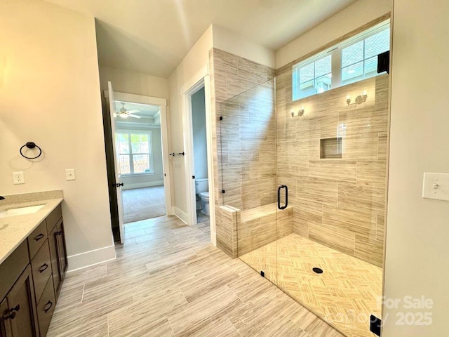 bathroom featuring vanity, toilet, baseboards, ceiling fan, and a shower stall