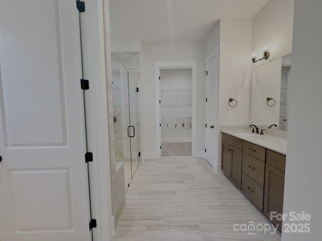 bathroom with vanity, baseboards, a shower stall, and a spacious closet