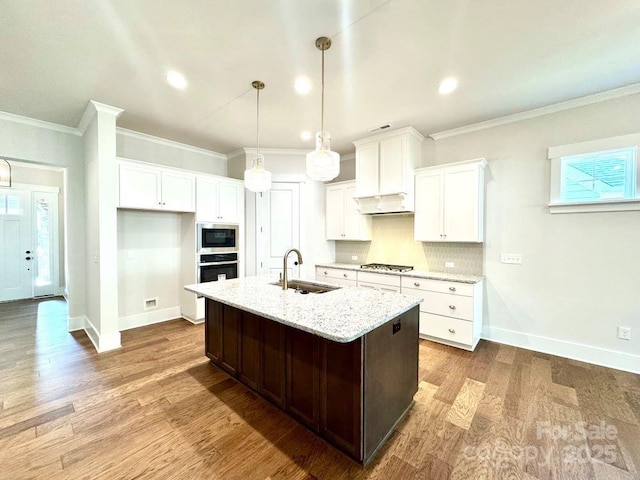 kitchen with a kitchen island with sink, stainless steel appliances, baseboards, and a sink