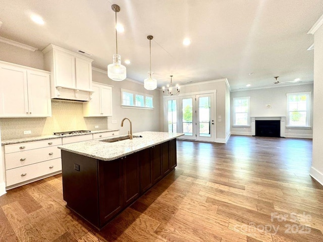 kitchen featuring a sink, crown molding, stainless steel gas cooktop, and a center island with sink