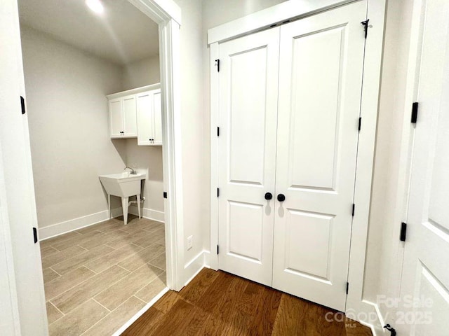 corridor featuring baseboards, a sink, and dark wood-style flooring