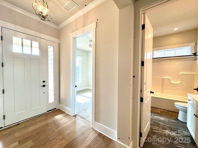 entryway with visible vents, crown molding, wood finished floors, baseboards, and a chandelier