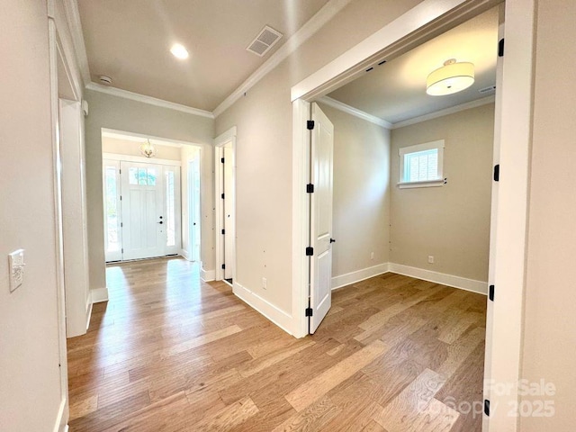 corridor featuring crown molding, baseboards, light wood finished floors, and visible vents