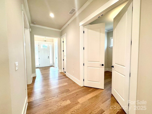 corridor with visible vents, ornamental molding, light wood finished floors, and baseboards