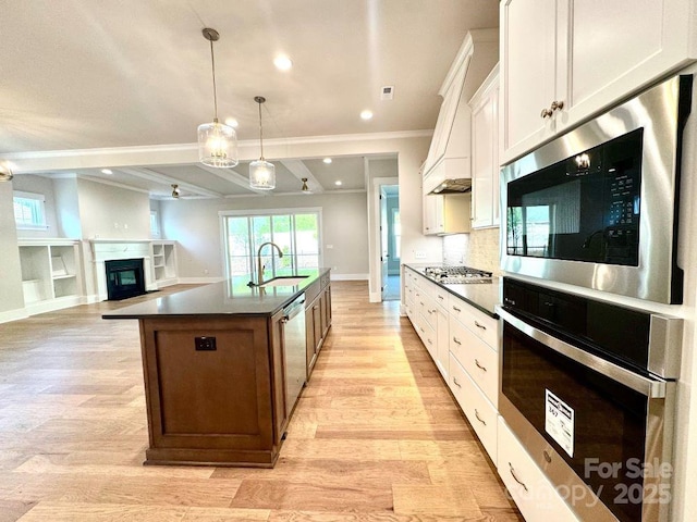 kitchen with a sink, dark countertops, light wood-style floors, and stainless steel appliances