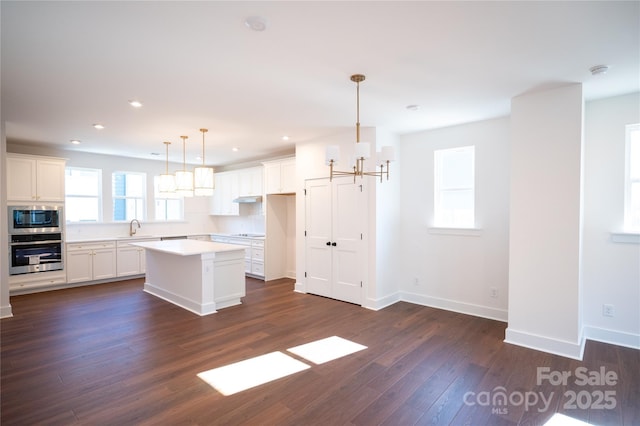 kitchen featuring stainless steel oven, dark wood-style floors, under cabinet range hood, built in microwave, and an inviting chandelier