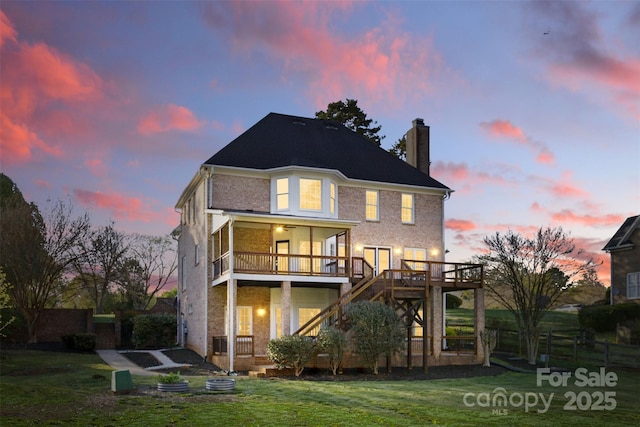 back of property featuring a chimney, a deck, stairs, and a lawn