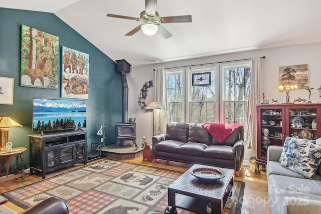 living room featuring vaulted ceiling, wood finished floors, a wood stove, and a ceiling fan